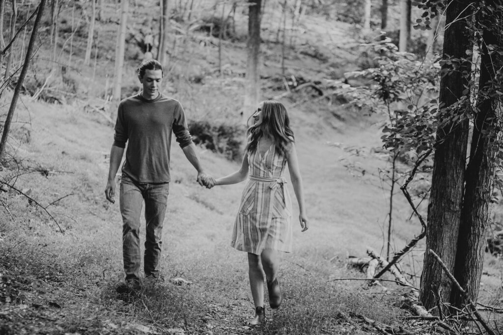 A black and white photo of a couple walking int he woods during their adventure engagement session
