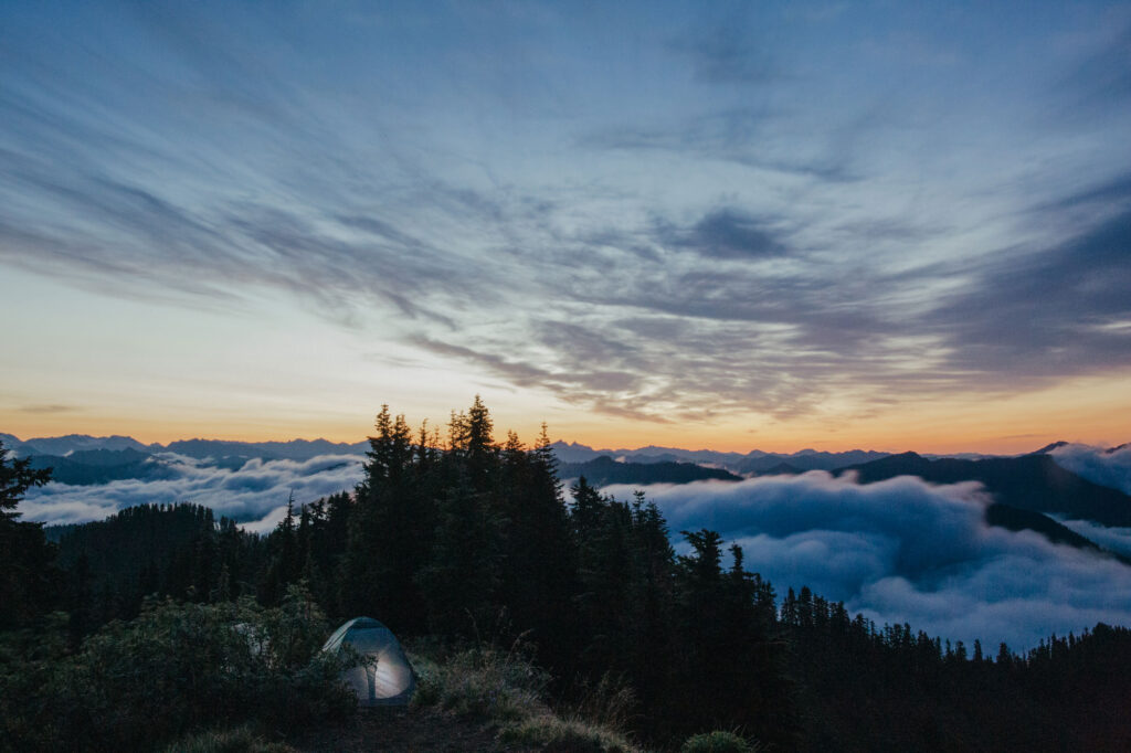 A lit up camping tent atop of a mountain as the sun sets