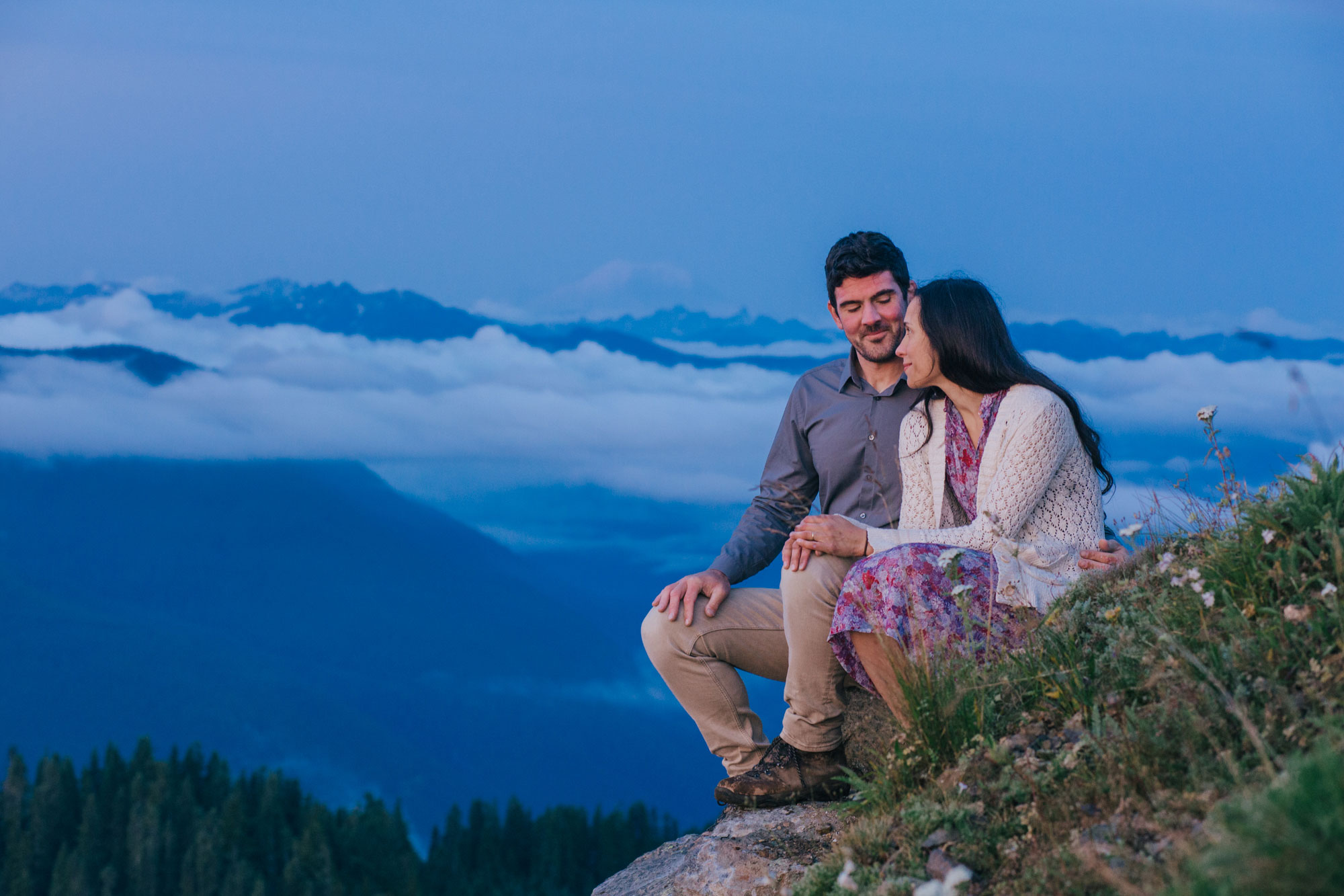 An adventurous couple sits on a hill while watching the sunrise  on the top of Evergreen Mountain Lookout in Washington