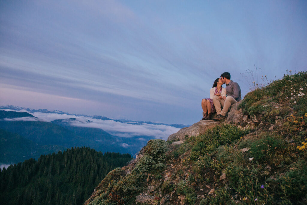 A husband and wife sit on the top of a hill during an Adventure Session outside of Seattle Washington during blue hour. 