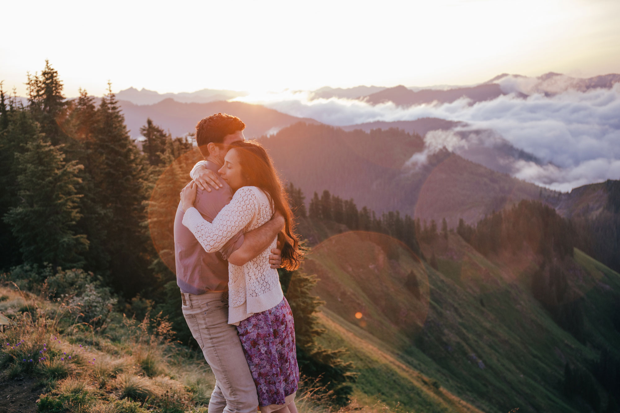 An adventurous couple hugging atop Evergreen Mountain at sunrise