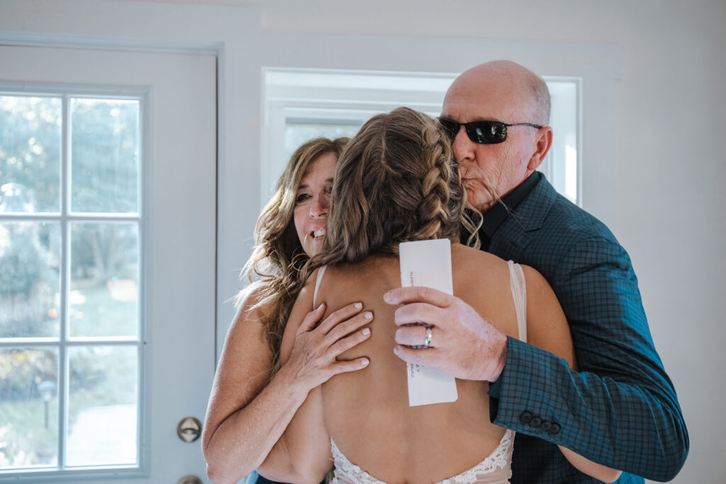 A bride embraces her mom and dad before walking down the aisle at her small backyard wedding. 