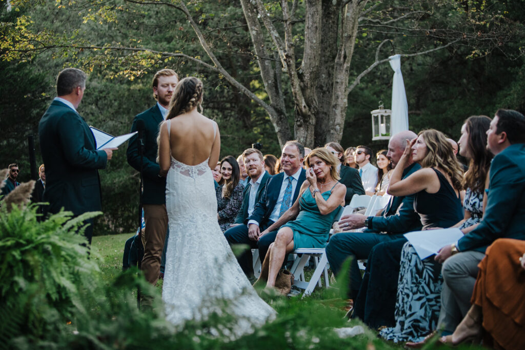 A wedding ceremony where you can see the guests. A woman in the front row is wiping away tears. The couple is facing each other holding hands. 