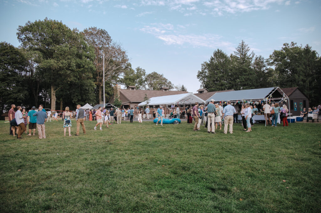 A photo of the guests at a campground wedding cocktail hour. Everyone is standing in the grass in casual clothing.