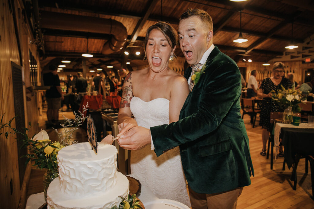 A bride and groom cut their cake at their wedding reception. Both of them have their mouths wide open