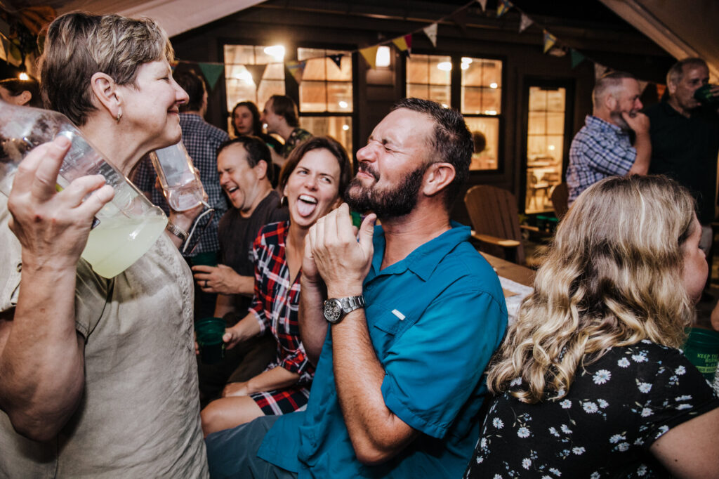 A woman reacts with a smile after a man swallows the tequila and mixer she just poured into his mouth. He is making a face, and she is laughing