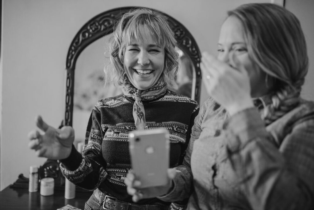 A brides friends are laughing hysterically at her while she poses in the bathtub on her wedding day.