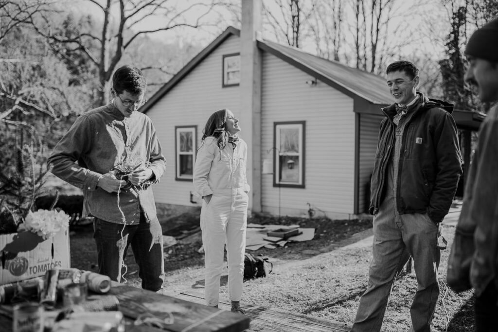 A bride dressed in a white jumpsuit  stands in front of her home before her and her friends walk across the street to her elopement ceremony location