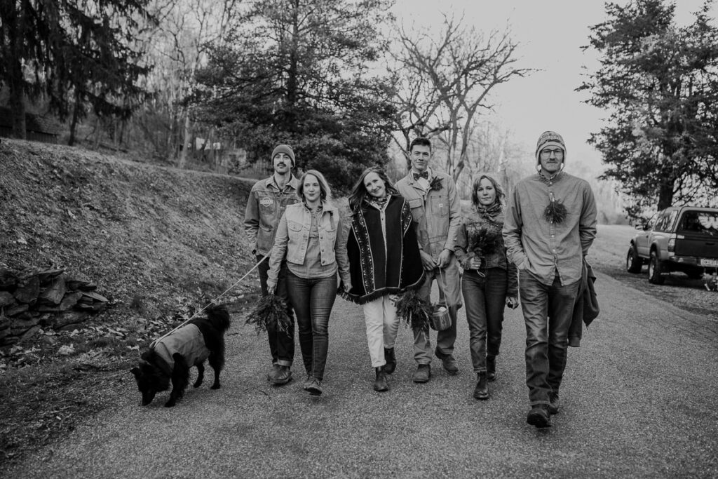 A black and white photos of a wedding party dressed in all denim, is walking down on a backroad on the way to their reception