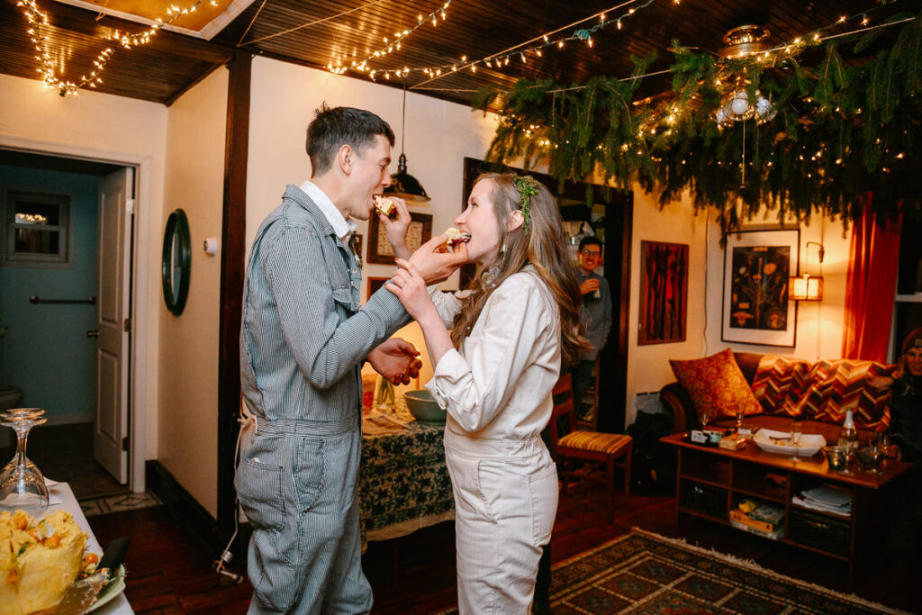 A bride and groom are feeding each other cake during their intimate reception inside their home. 