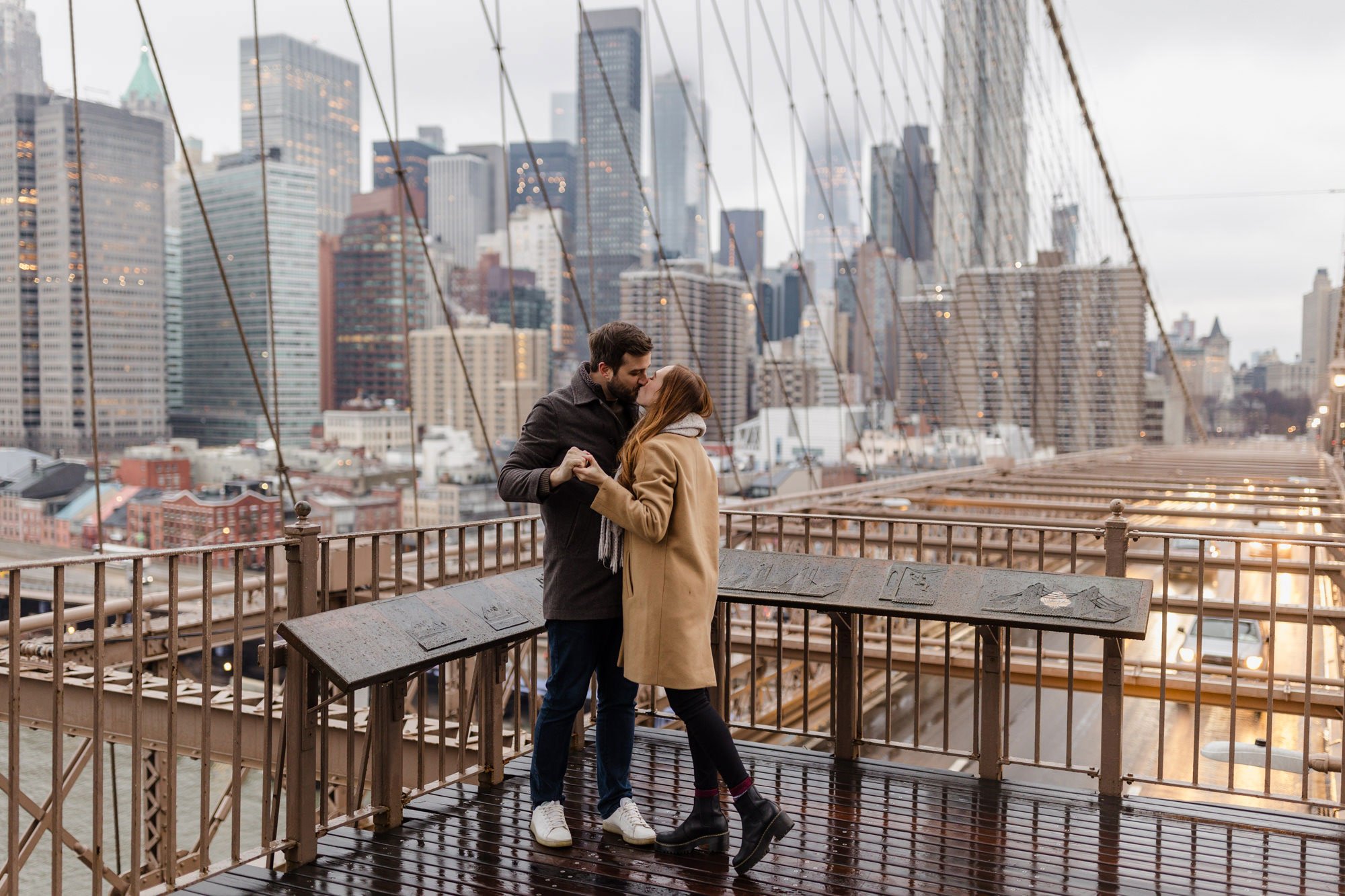 An engaged couple standing while holding hands on the corner of the Brooklyn Bridge