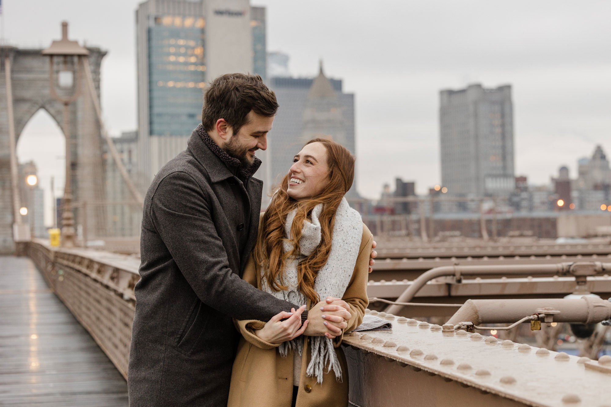 Engaged couple smiling at each other on the Brooklyn Bridge