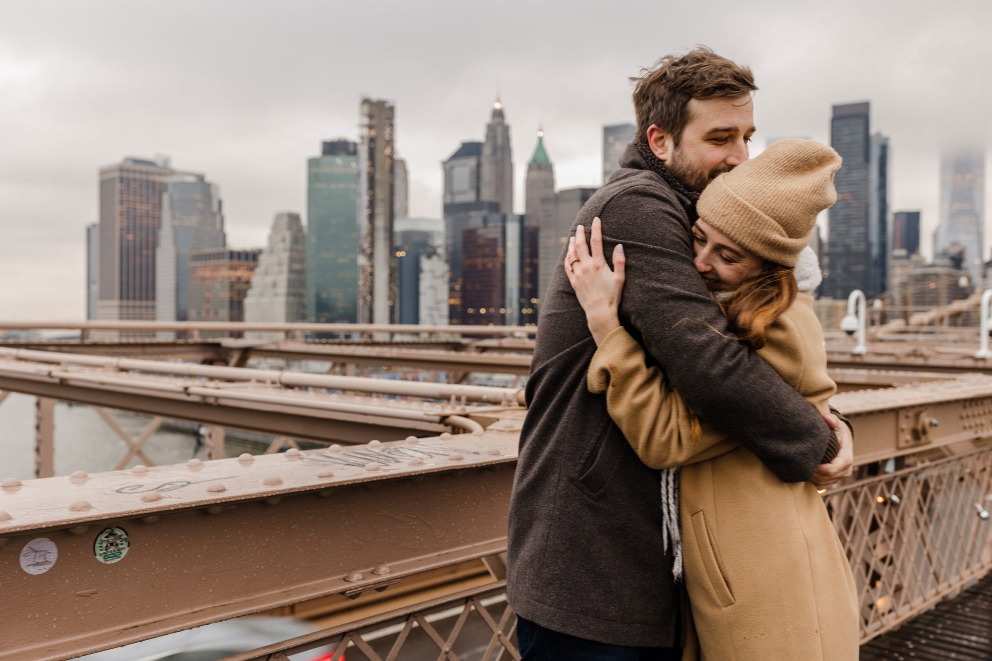 An engaged couple embracing on the Brooklyn Bridge