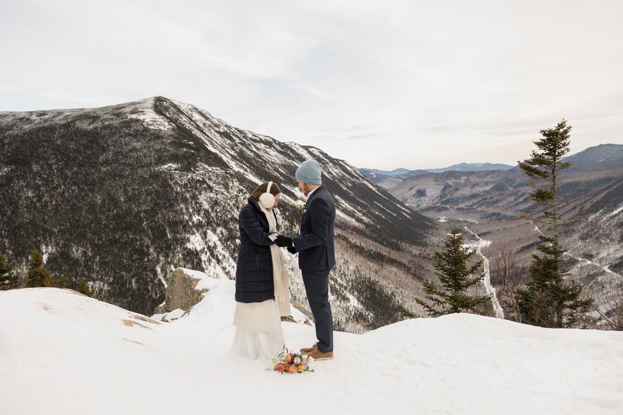 A couple stands at the top of a mountain during their elopement. They are exchanging vows in the snow. 