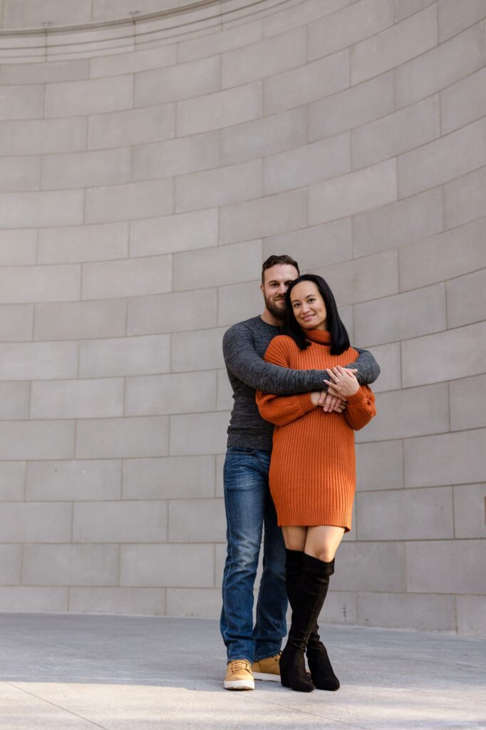 An engaged couple poses in front of Naumberg Bandshell in Central Park