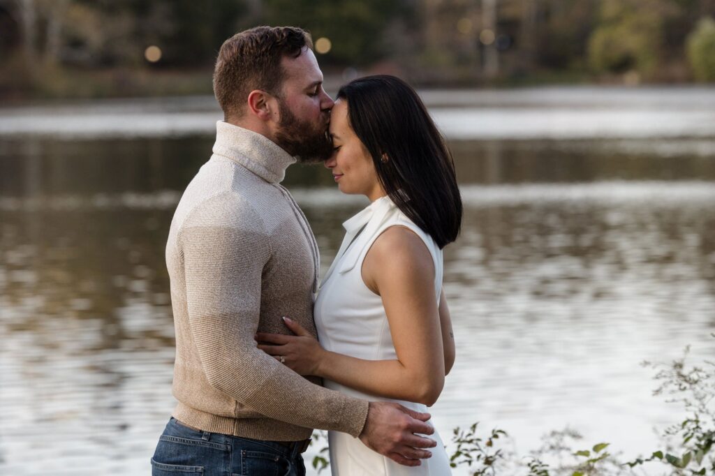 A man and woman face each other. He is kissing her forehead. They both have their eyes closed.