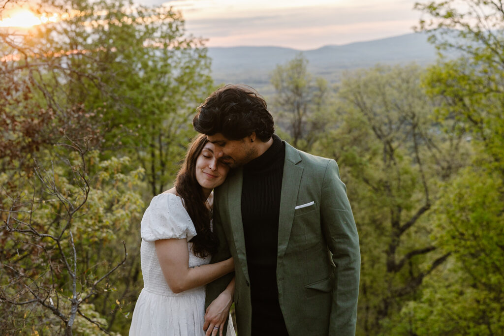 A bride leans on her groom and snuggles in, and they enjoy a sunrise on their elopement day