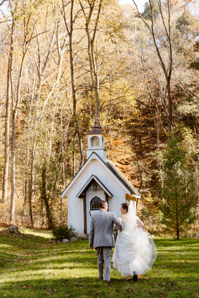 A bride and groom walking arm in arm towards the intimate chapel at Drumore Mill. The couple is looking at one another and smiling, and the bride is holding up the layers of her dress.