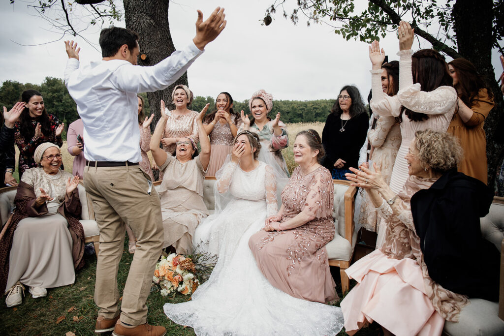 During the Bedeken at a wedding, the bride and groom see one another for the first time in seven days. The groom has his hands up, and the bride is covering her mouth with excitiment. 