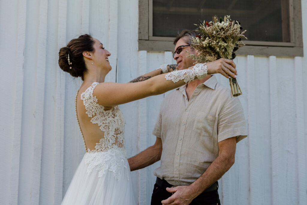 The bride shares a sweet moment with her dad when he sees her for the first time on her elopement day. She is wearing an a-line dress with a sheer bodice and sleeves