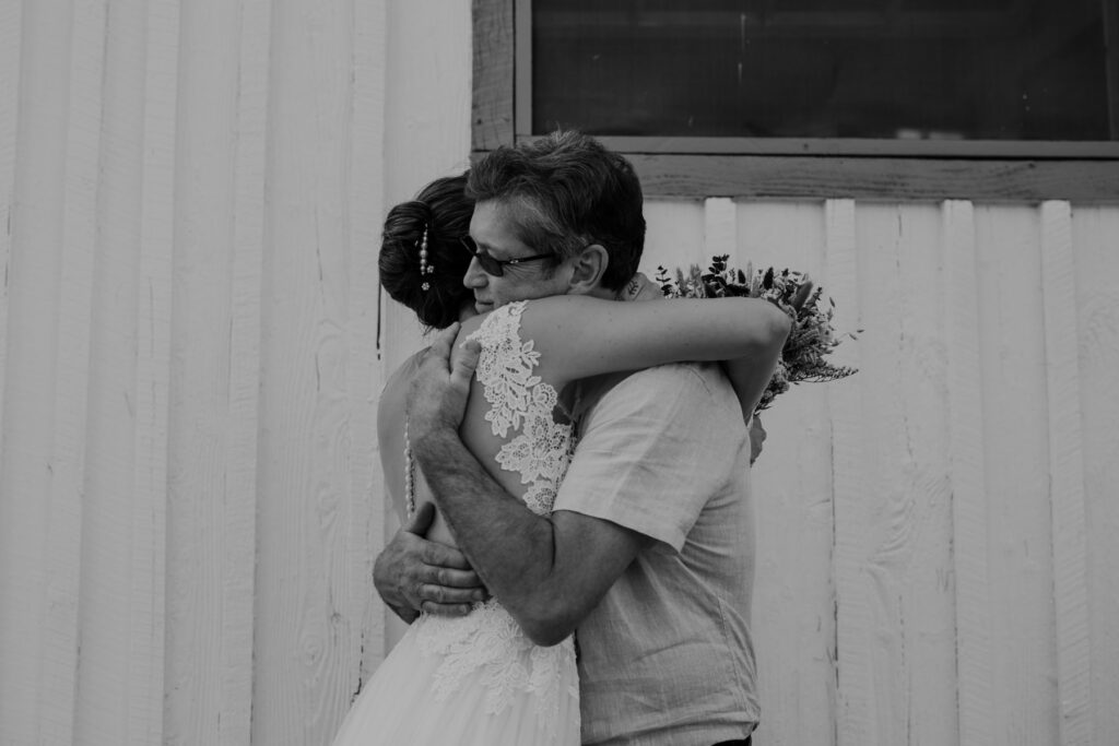 The bride and her dad embrace when he sees her for the first time on her elopement day. She is wearing an a-line dress with a sheer bodice and sleeves. 