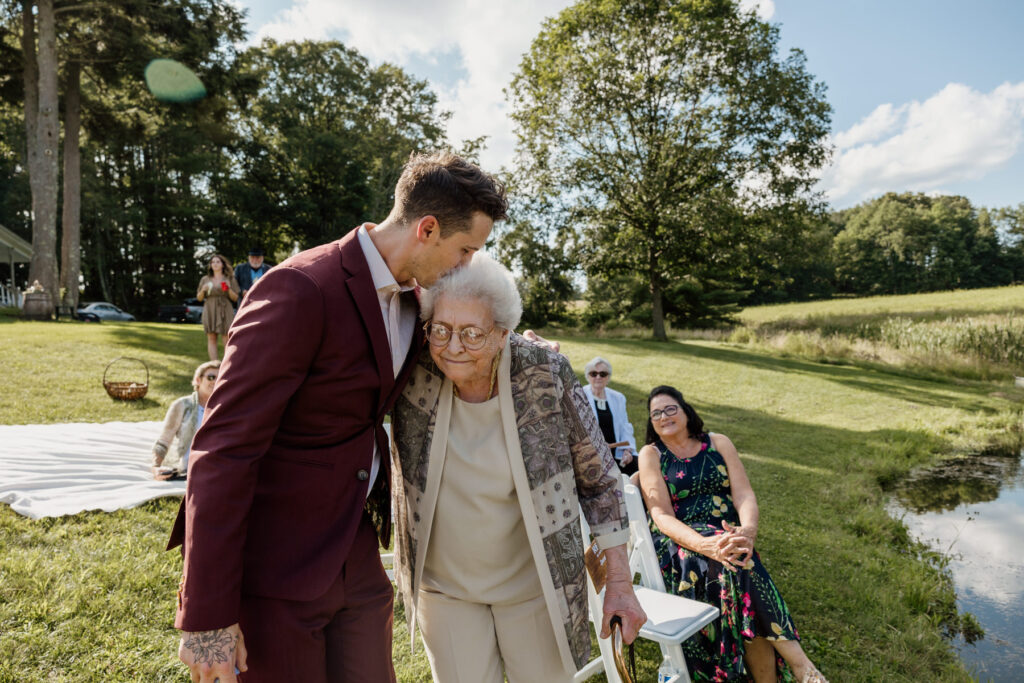 A groom kisses the brides grandma on the forehead as he walks to the ceremony on his elopement day 