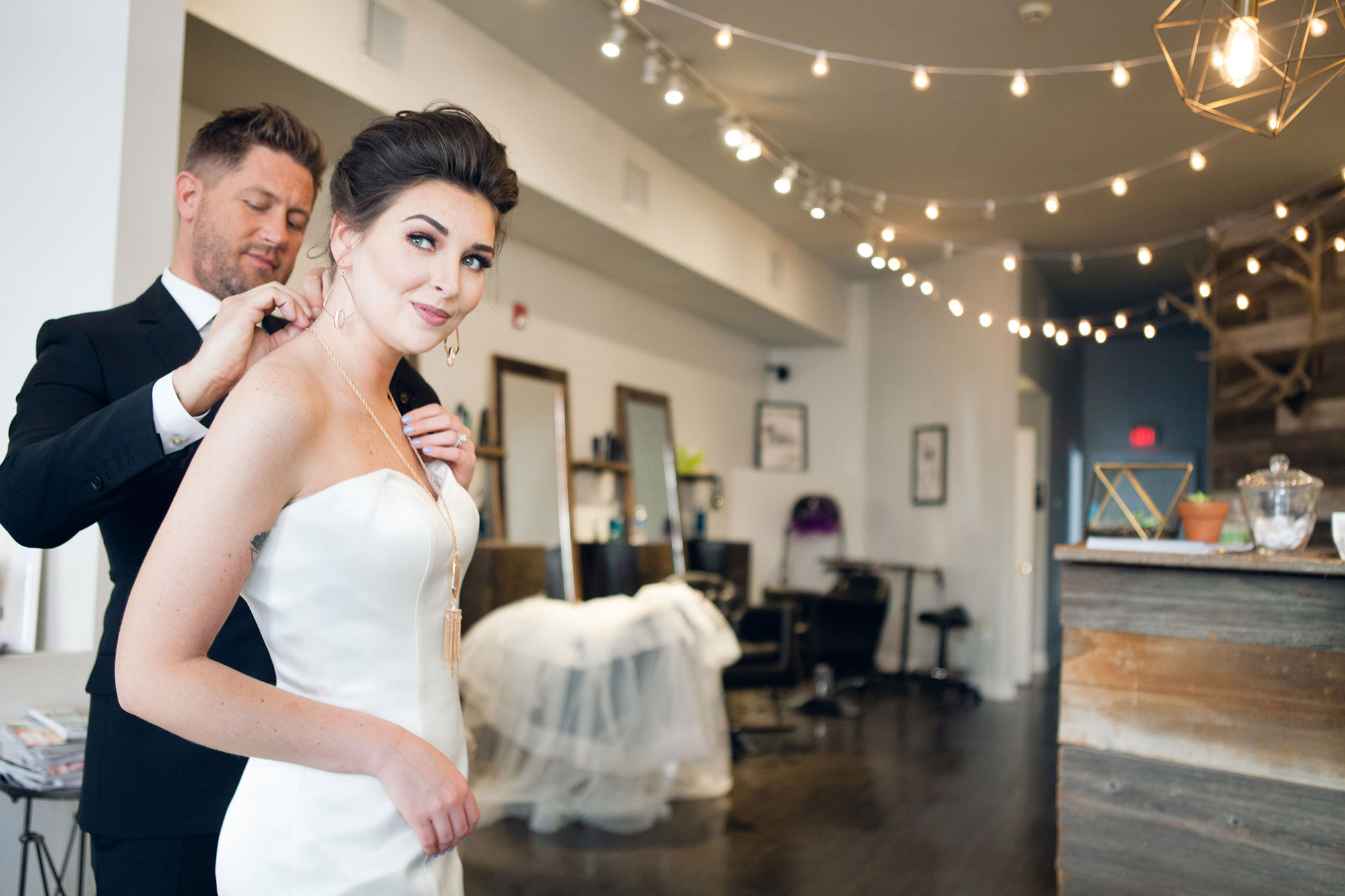 a groom helps his bride get ready on their wedding day