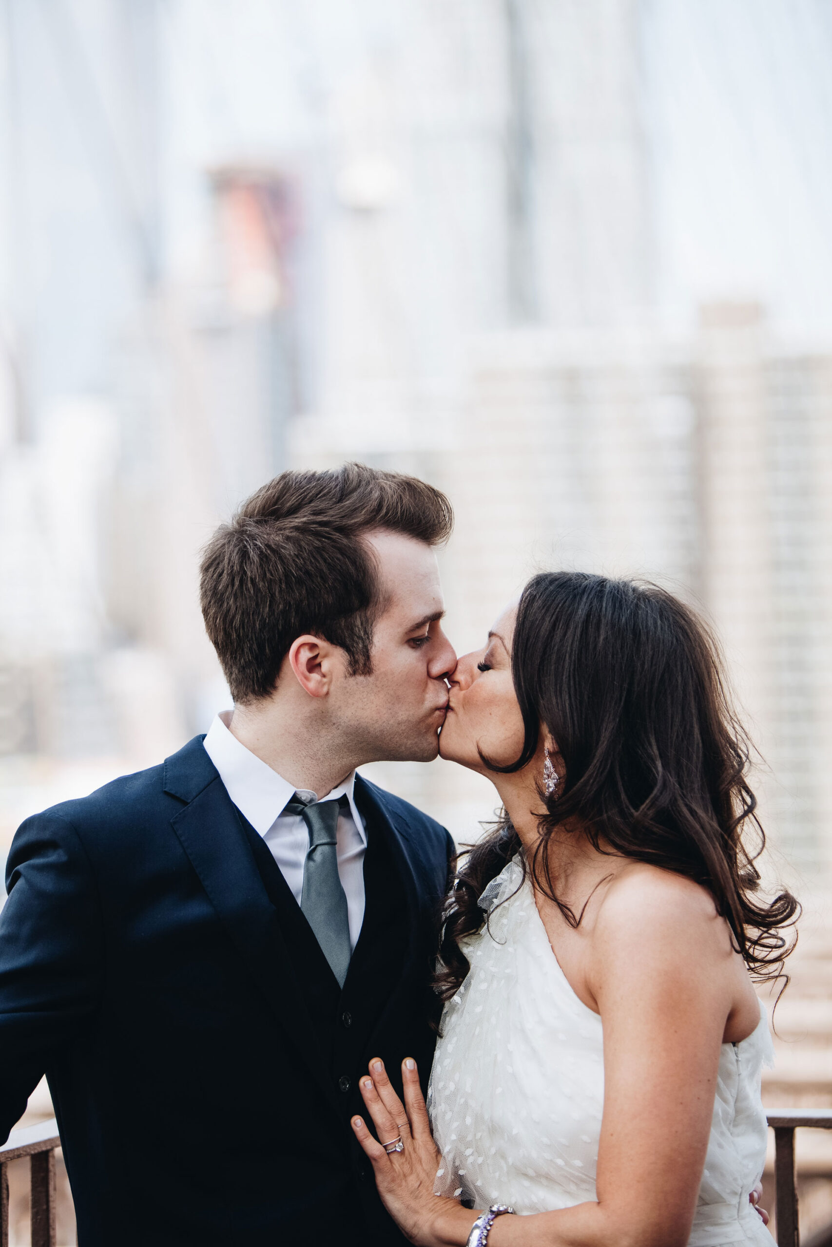 A bride and groom being photographed kissing on the Brooklyn Bridge