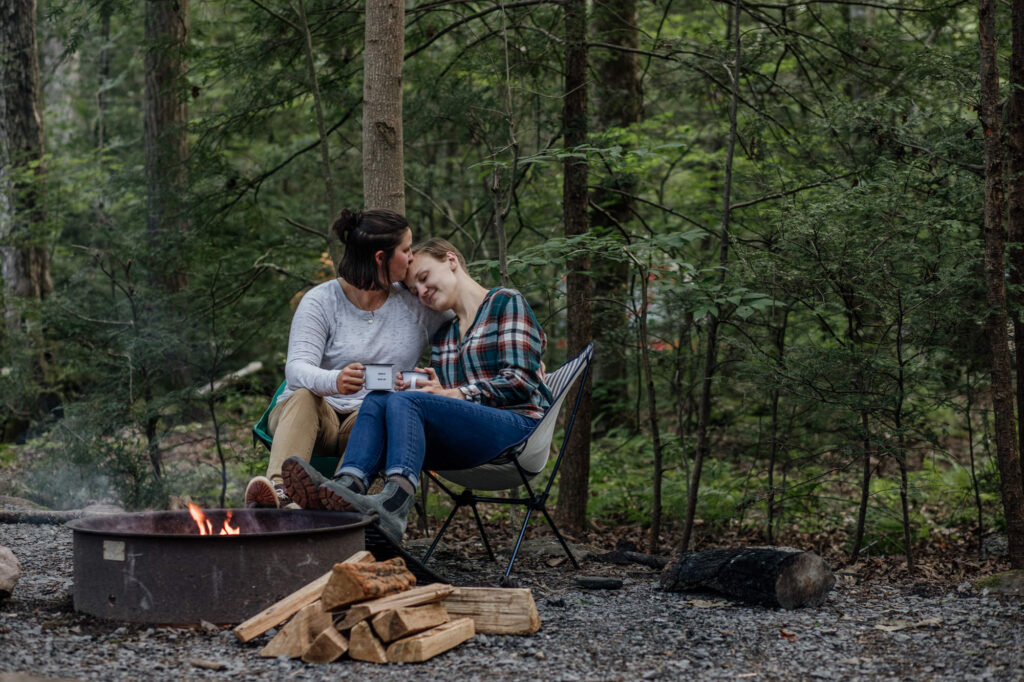 couple snuggling by a fire pit while drinking coffee