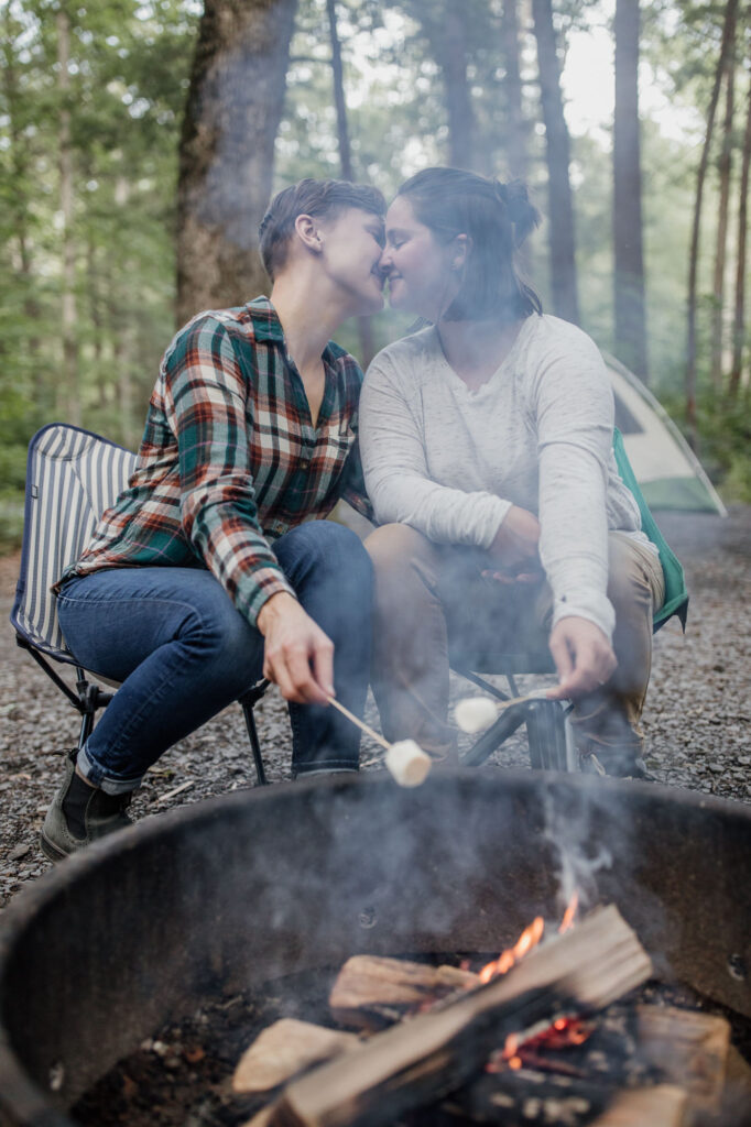 same sex couple kissing while roasting marshmallows by the fire during their engagement session