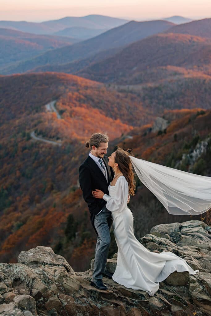 A bride and groom stand at an overlook at sunrise during their elopement