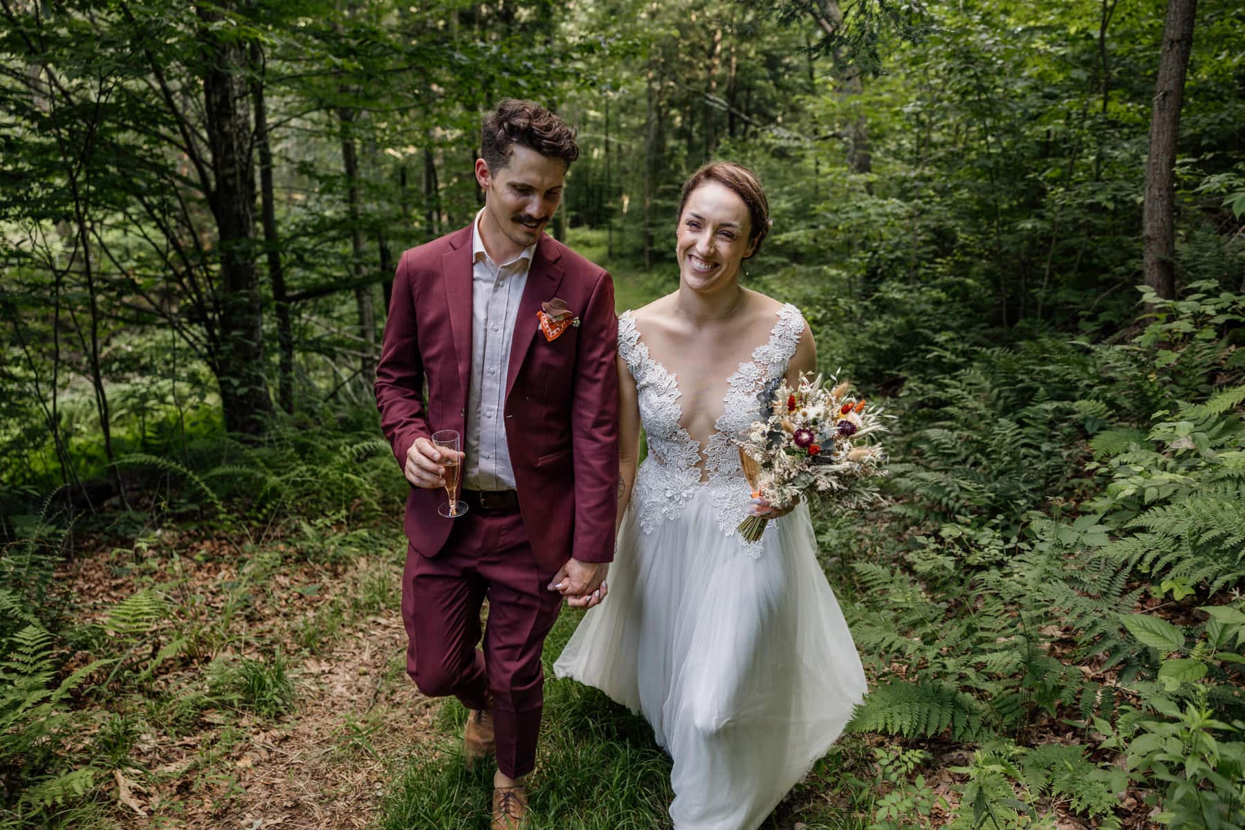 A bride and groom walk through the forest laughing and smiling