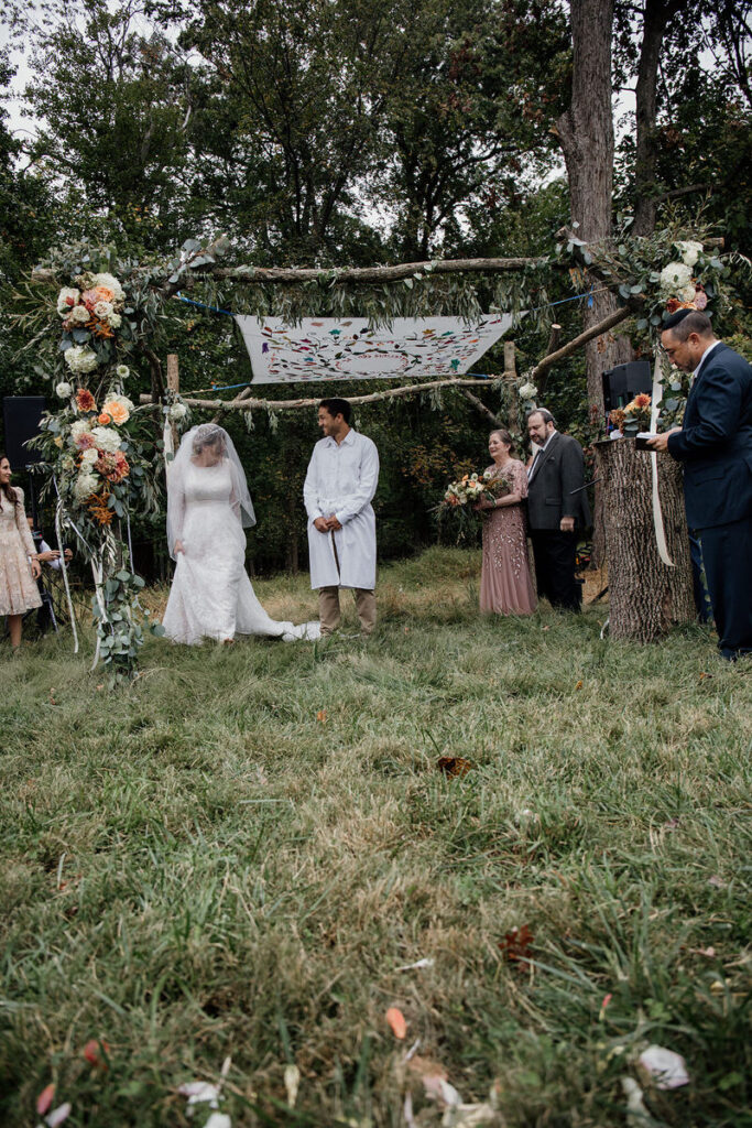 A bride and groom under a canopy made of tree branches and colorful flowers