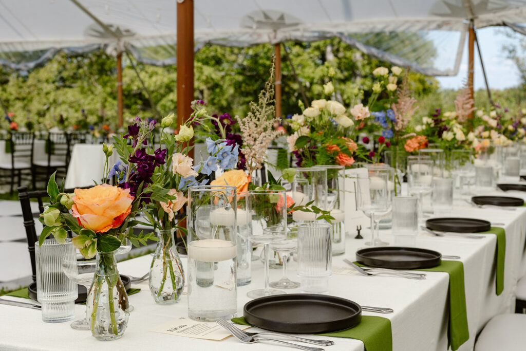 A photo of a table scape at a wedding reception. There are roses, and wildflowers. There are also modern black plates with green napkins