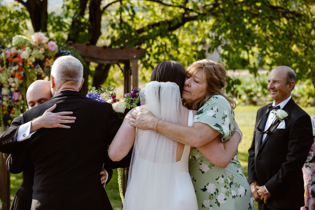 A mother and father hug the Bride and Groom during an intimate wedding ceremony. 