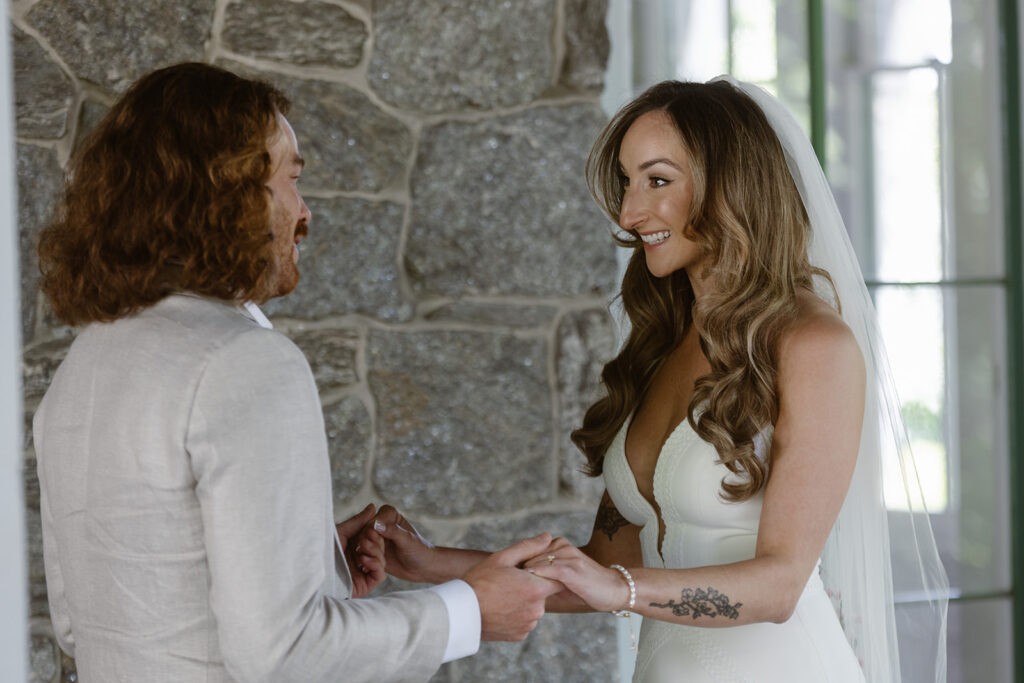 A bride look elated as she sees her groom for the first time during their first look. The couple is holding hands, and are standing in front of an old stone mansion