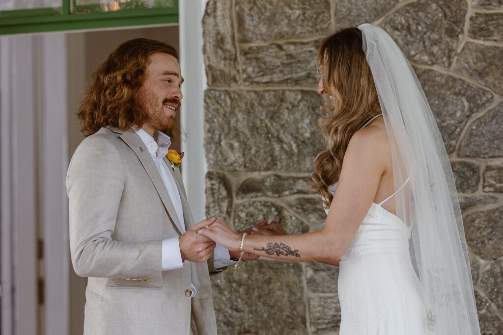 A groom tears up as he sees his bride during their first look. The couple is holding hands, and are standing in front of an old stone mansion