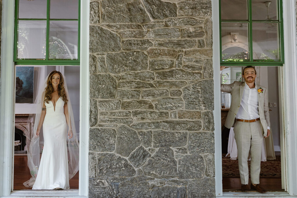 A bride and groom standing in the floor to ceiling windows of a victorian mansion