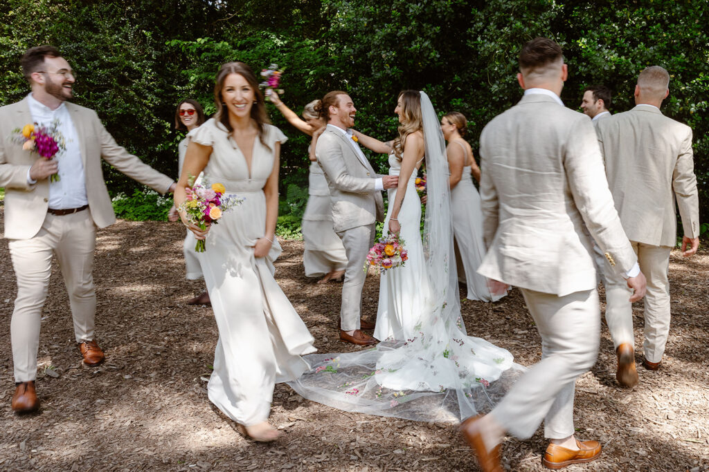 A bride and groom standing in the middle of their bridal party. The bridal party is circling the couple. The men are wearing cream linen suits, and the women are wearing cream dresses