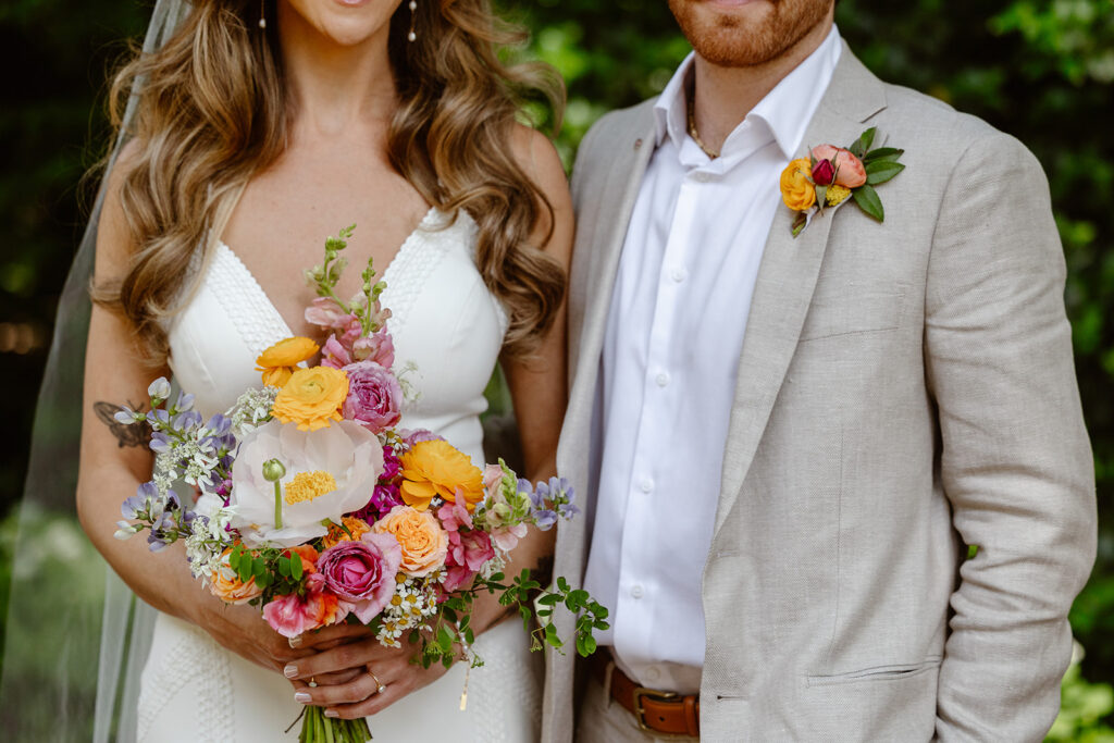 A closeup of the details of the bride and grooms outfits on their wedding day. The bride is holding a beautiful bouquet including poppies, ranunculus, and wildflowers. 