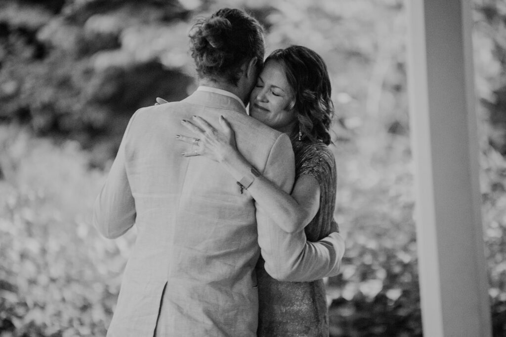 A black and white photo of the groom  dancing with his mother.  They are dancing cheek to cheek, and the moms eyes are closed with emotion