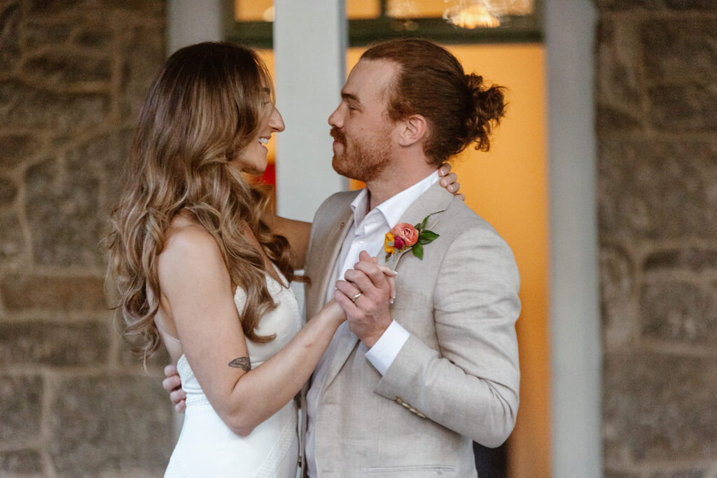 A bride and groom during their first dance  on their wedding day. They are smiling at one another.