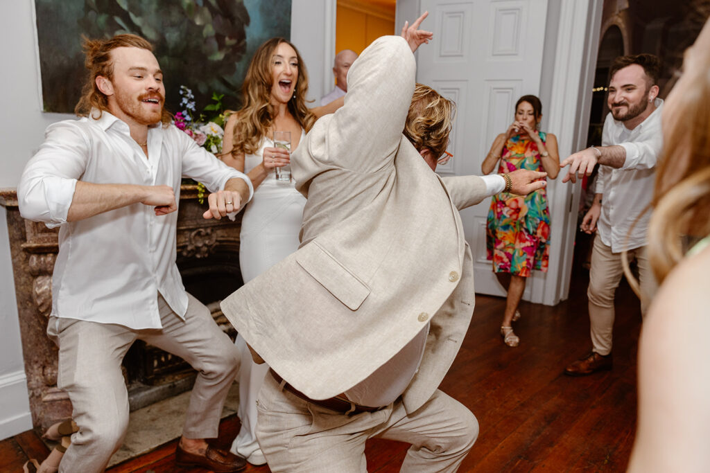 The bride and groom dancing with the grooms dad during their reception. They are dancing in a gallery space with paintings on the wall