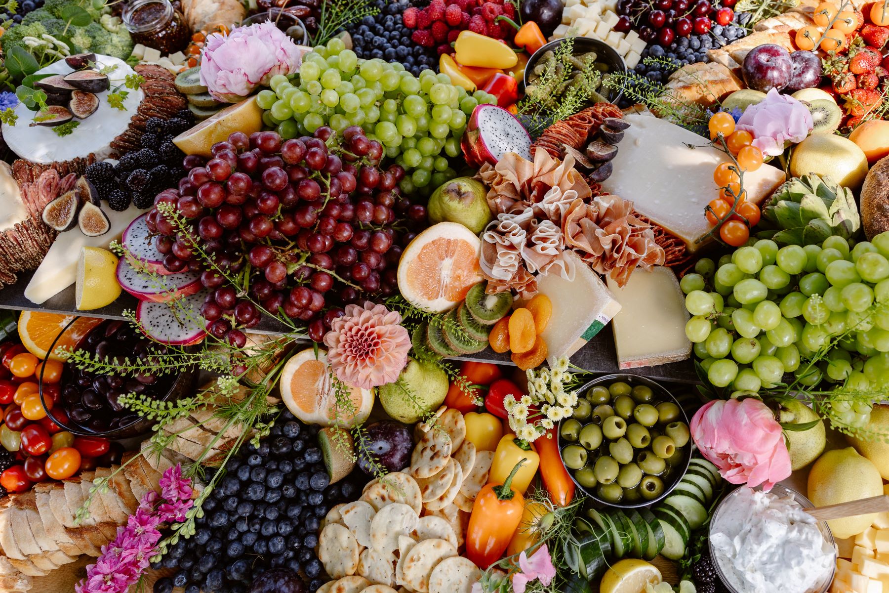 A large charcuterie board with fuits, vegetables, dips, crackers, and cheese