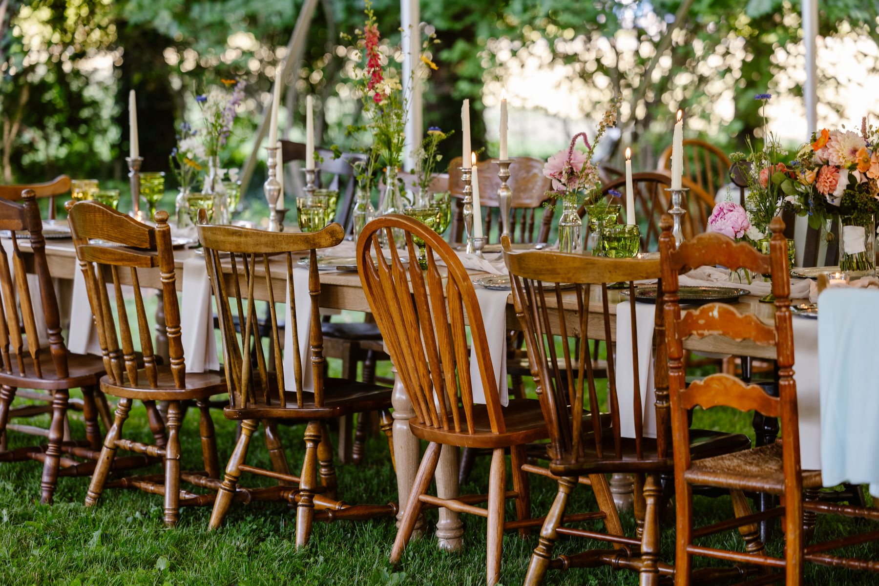 Wooden chairs, a long wooden table covered in plants and flowers in vases and candles