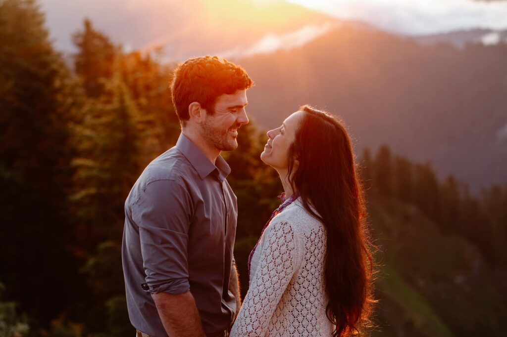 A couple embraces at the top of a mountain during their elopement. The sun is just rising behind them, and it is creating a dramatic effect