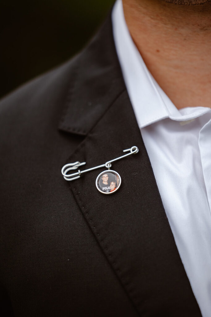 A closeup of a pin a groom is wearing. It has a photo of him and his mother.