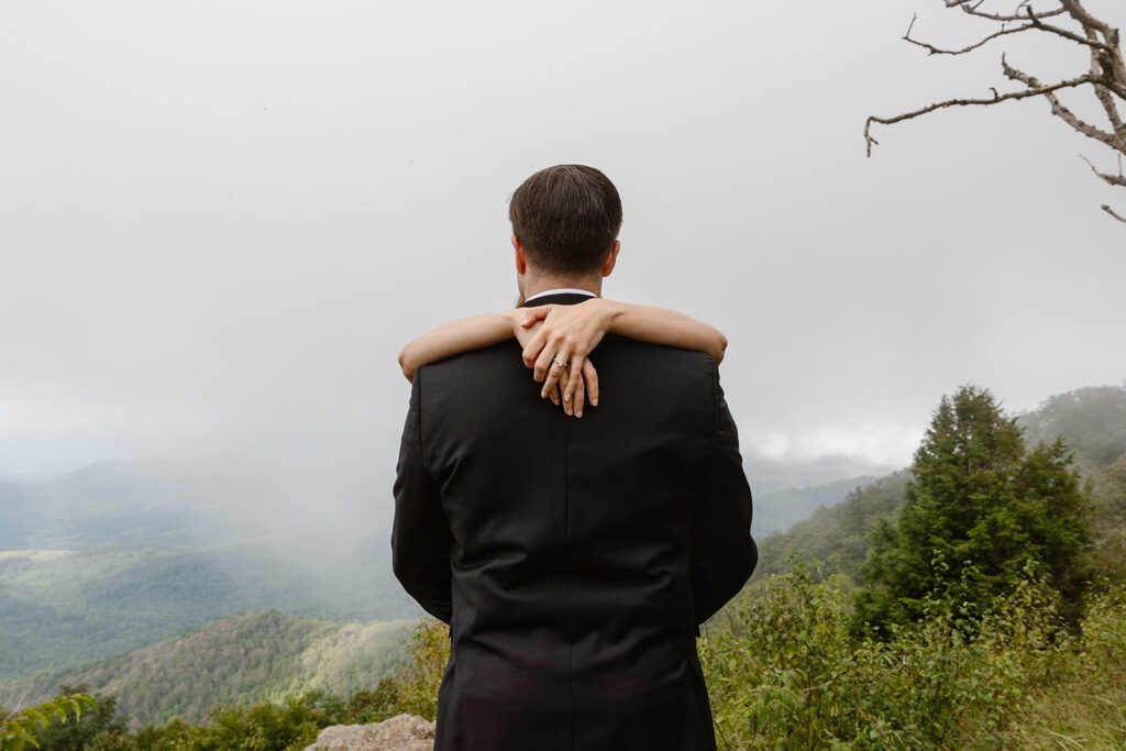 You see the grooms back, and the hands of the bride are wrapped around his shoulders and resting on his neck