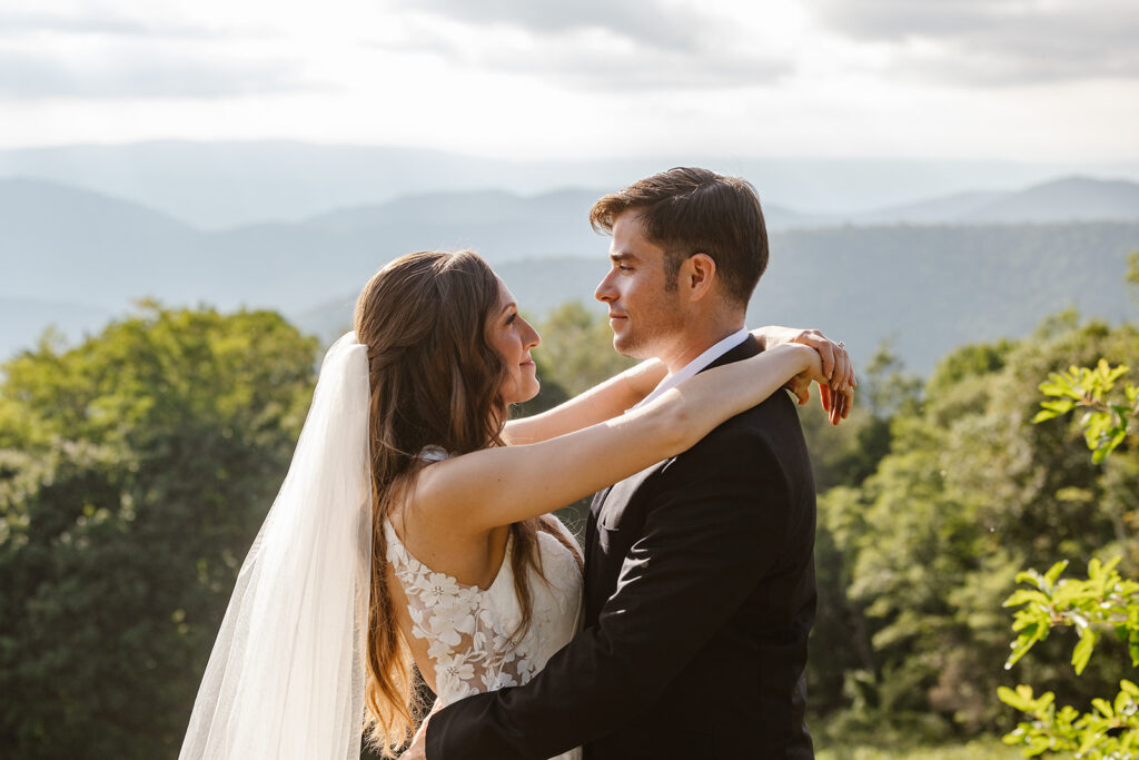 A bride and groom facing each other in front of the mountains. The bride has her arms resting on the grooms shoulders.