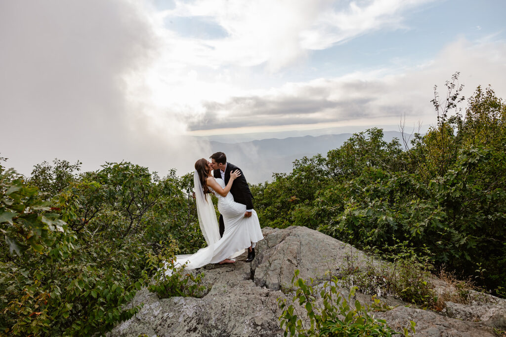 A bride and groom dip kissing at Bearfence Mountain overlook. 